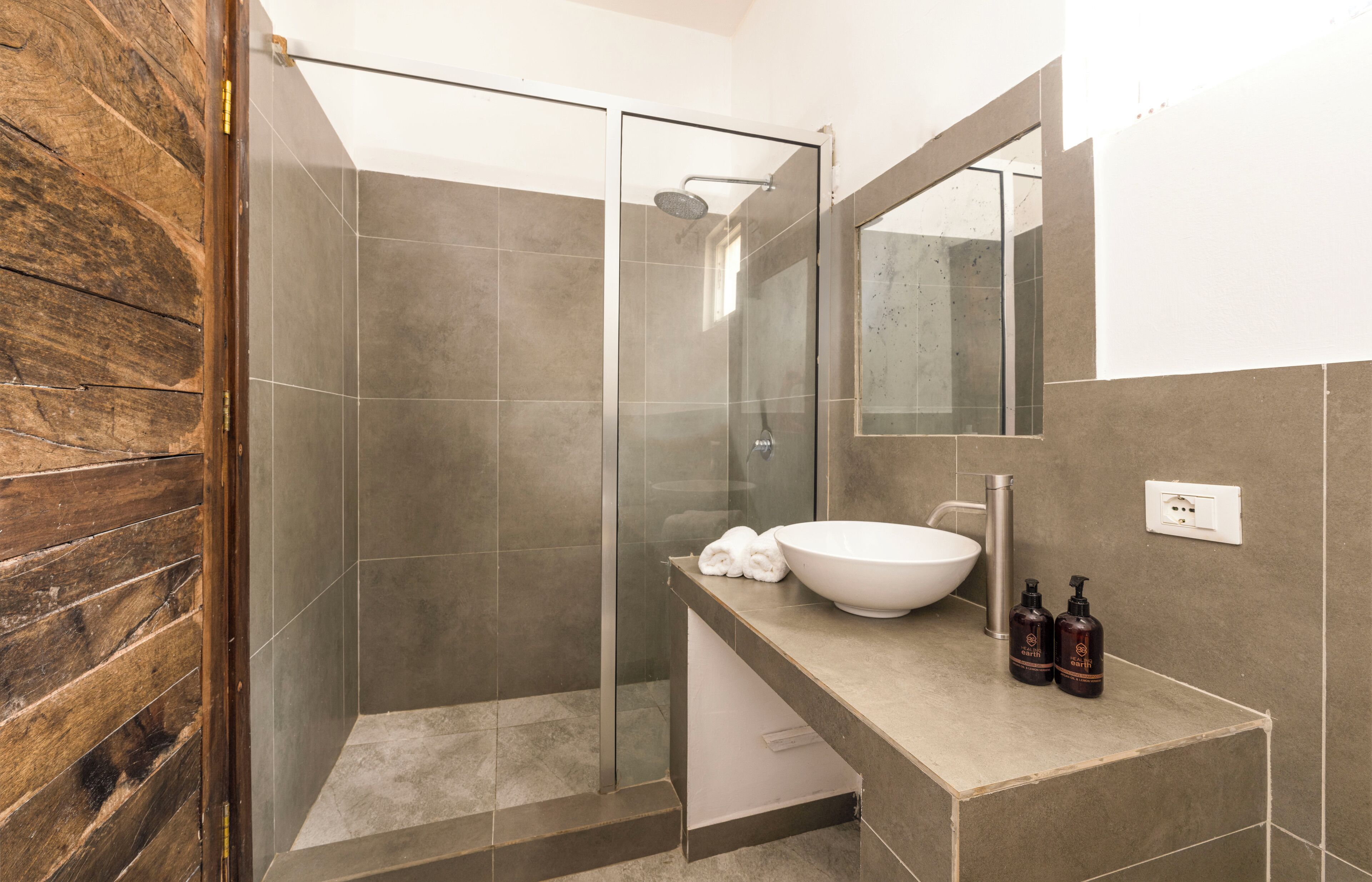 A modern bathroom with a glass-enclosed shower, a large white sink, and two bottles of shampoo on the countertop.