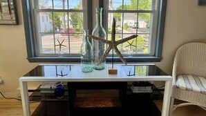 A room with a white console table, a wicker chair, and a view through a window with two starfish decorations. - Sandy Toes Retreat (Ogunquit)