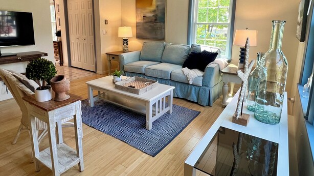 A living room with a sofa, coffee table, TV, and decorative items. - Sandy Toes Retreat (Ogunquit)