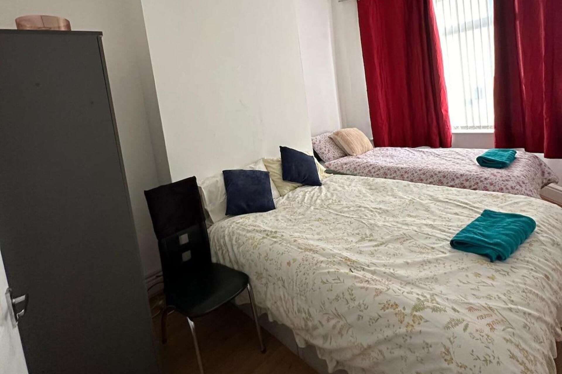 A bedroom with two beds, a chair, and a wardrobe.