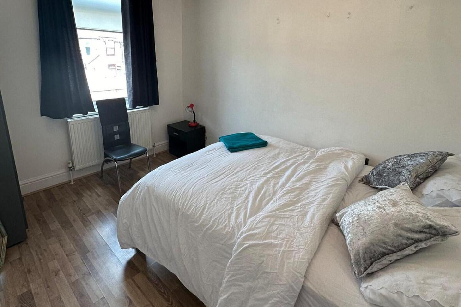 Une chambre à coucher avec un lit, une chaise, un radiateur et une fenêtre avec des rideaux.