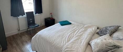 A bedroom with a bed, a chair, a radiator, and a window with curtains.