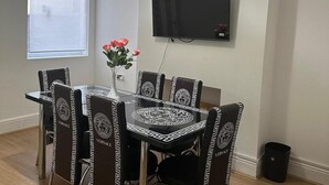 Een eetruimte met een glazen tafel en stoelen met een zwart-wit geometrisch patroon. Op tafel staat een vaas met roze bloemen.