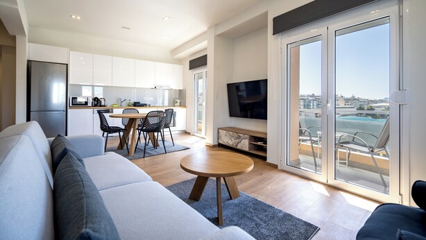 A modern living room with a sofa, a dining table with chairs, a TV, and large sliding glass doors to a balcony. - Attiki Square & Metro Modern 2-Bedroom Apt by MPS (Athina)
