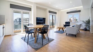 A modern living room with a dining area, large windows, and a flat-screen TV. - Attiki Square & Metro Modern 2-Bedroom Apt by MPS (Athina)
