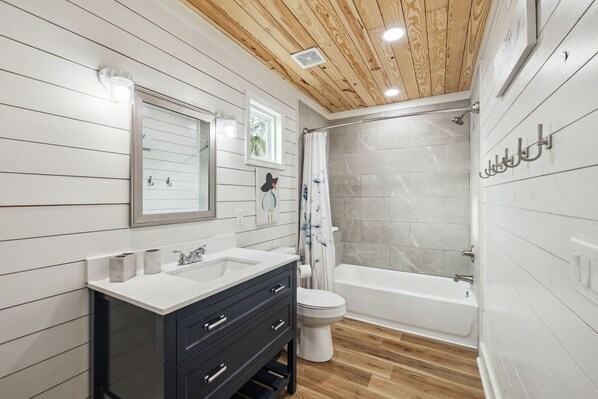 A modern bathroom with a wooden ceiling, white walls, a large mirror, a vanity with a sink, a toilet, and a bathtub.