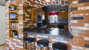 Una cucina con zoccolo in mattoni, mobili in legno, piano di lavoro nero e angolo bar integrato con sgabelli.