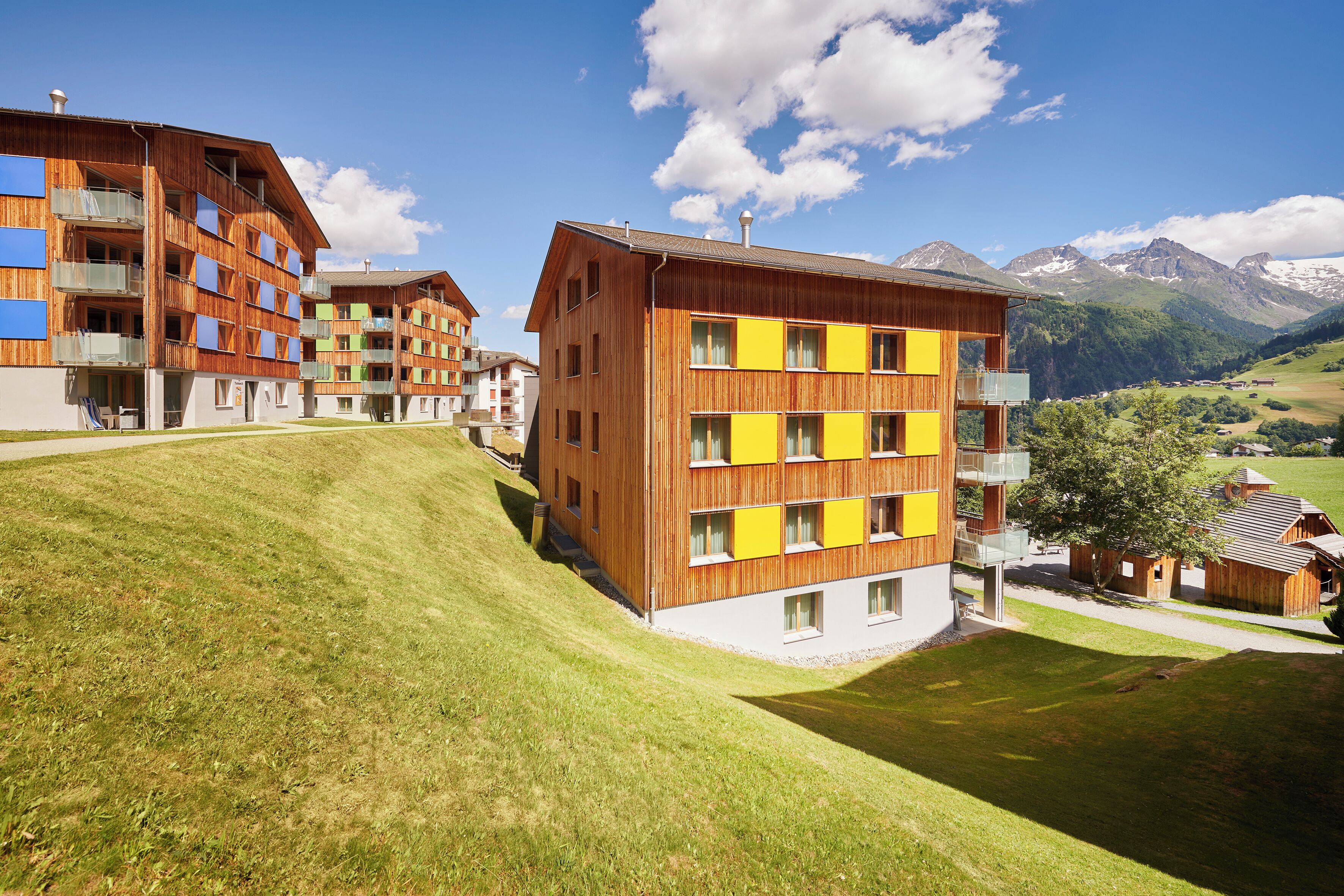 Un hôtel moderne à plusieurs étages, doté de balcons et offrant une vue sur les montagnes en arrière-plan.