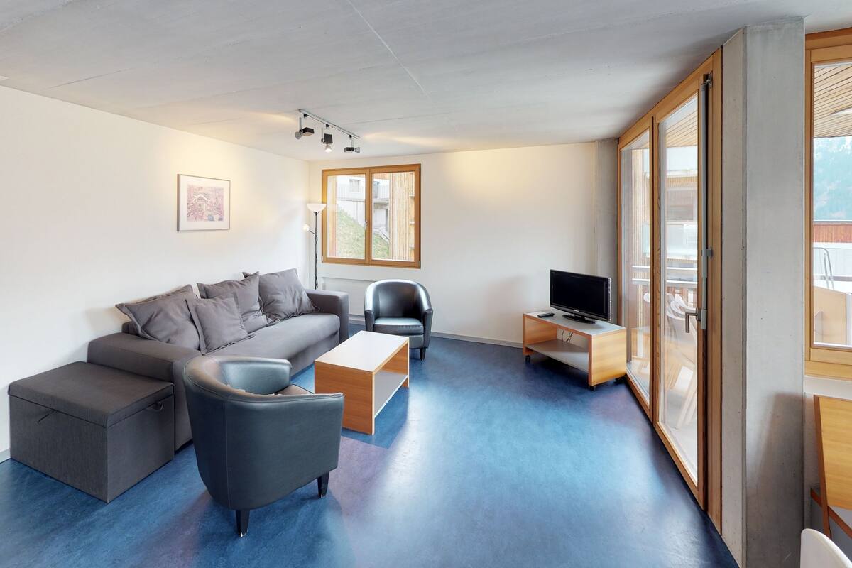 A modern living room with a grey sofa, a black armchair, a wooden coffee table, and a TV on a wooden stand.