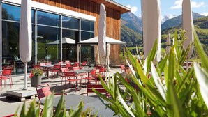 An outdoor seating area with red chairs and white umbrellas, overlooking a mountainous landscape. - Reka-Feriendorf Disentis (Disentis)