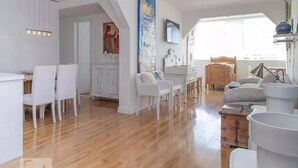 A spacious living area with a wooden floor, white furniture, and a dining area with a white cabinet and chairs. - Barra da Tijuca 2 Bedroom Apartment on the Beach (Rio de Janeiro)