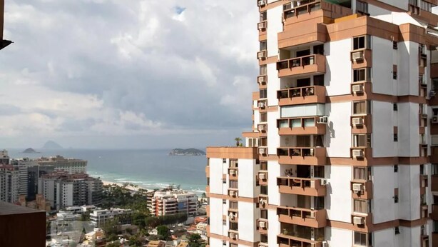 A high-rise building with multiple balconies, overlooking a coastal area with buildings and a beach. - Barra da Tijuca 2 Bedroom Apartment on the Beach (Rio de Janeiro)