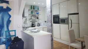 A modern kitchen with white cabinets, a microwave, and a coffee maker. There is a blue vase on a shelf and a blue chair in the dining area. - Barra da Tijuca 2 Bedroom Apartment on the Beach (Rio de Janeiro)