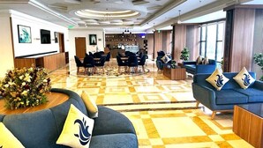 Un hall de hotel con piso de cuadros, zonas de estar, un mostrador de recepción y obras de arte en las paredes.