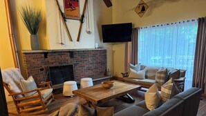 A cozy living room with a brick fireplace, comfortable seating, and a flat-screen TV mounted on the wall. - BirchView Trail *HOT TUB  (blue mountain)