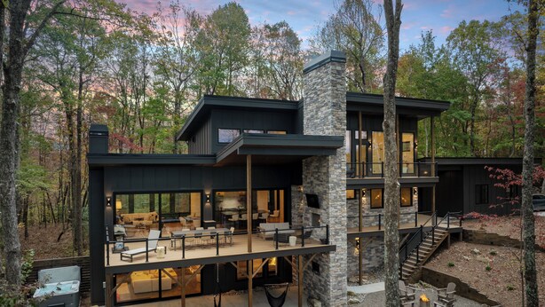 Une maison moderne à deux étages, avec une façade en pierre, de grandes fenêtres et un vaste espace extérieur aménagé en patio.