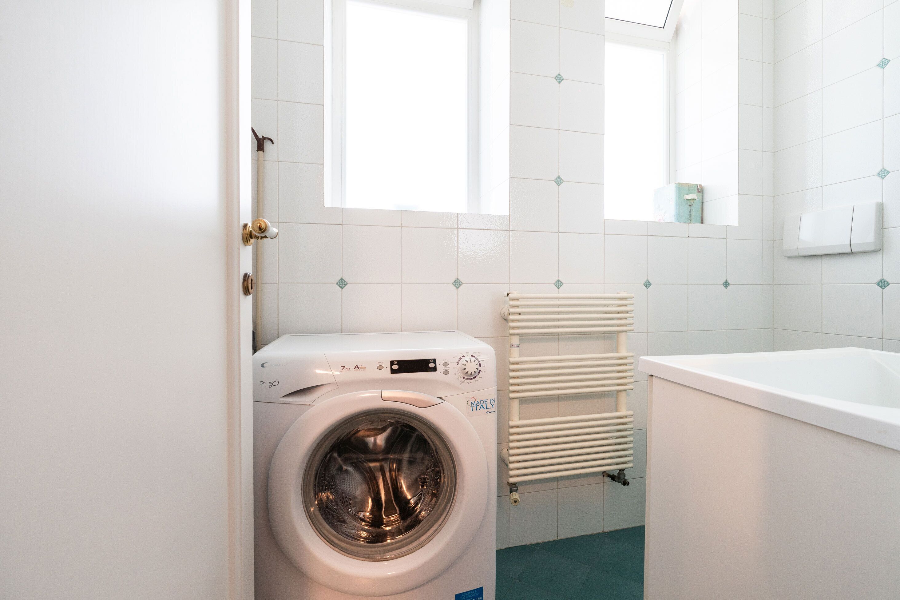 Ein kleines, modernes Badezimmer mit Waschmaschine, Badewanne und Handtuchhalter.