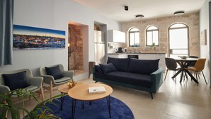 Un salon moderne avec un canapé, des fauteuils, une table basse et un tableau représentant un paysage urbain.