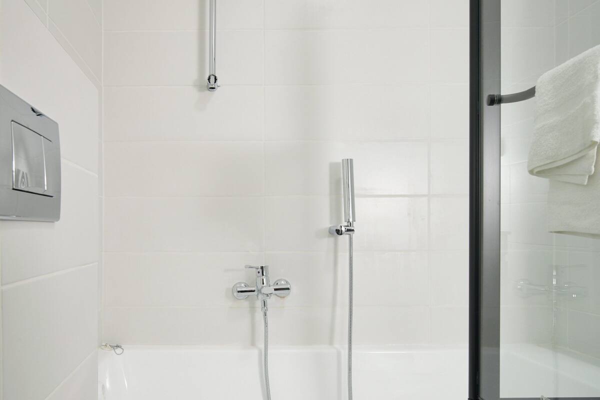 Een moderne badkamer met een douchecabine van glas, een witte badkuip en een toilet.