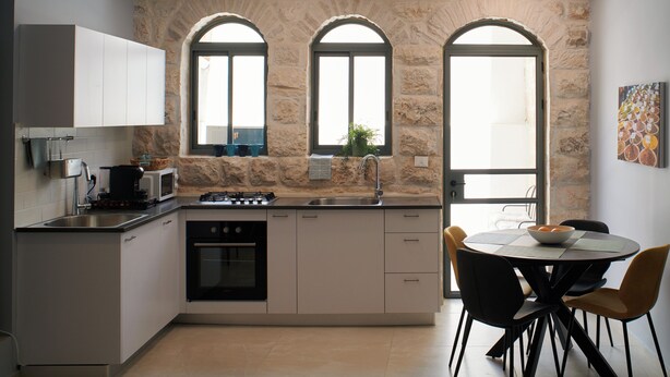 Une cuisine moderne avec un mur en pierre, un four encastré, un évier et un coin repas comprenant une table et des chaises.