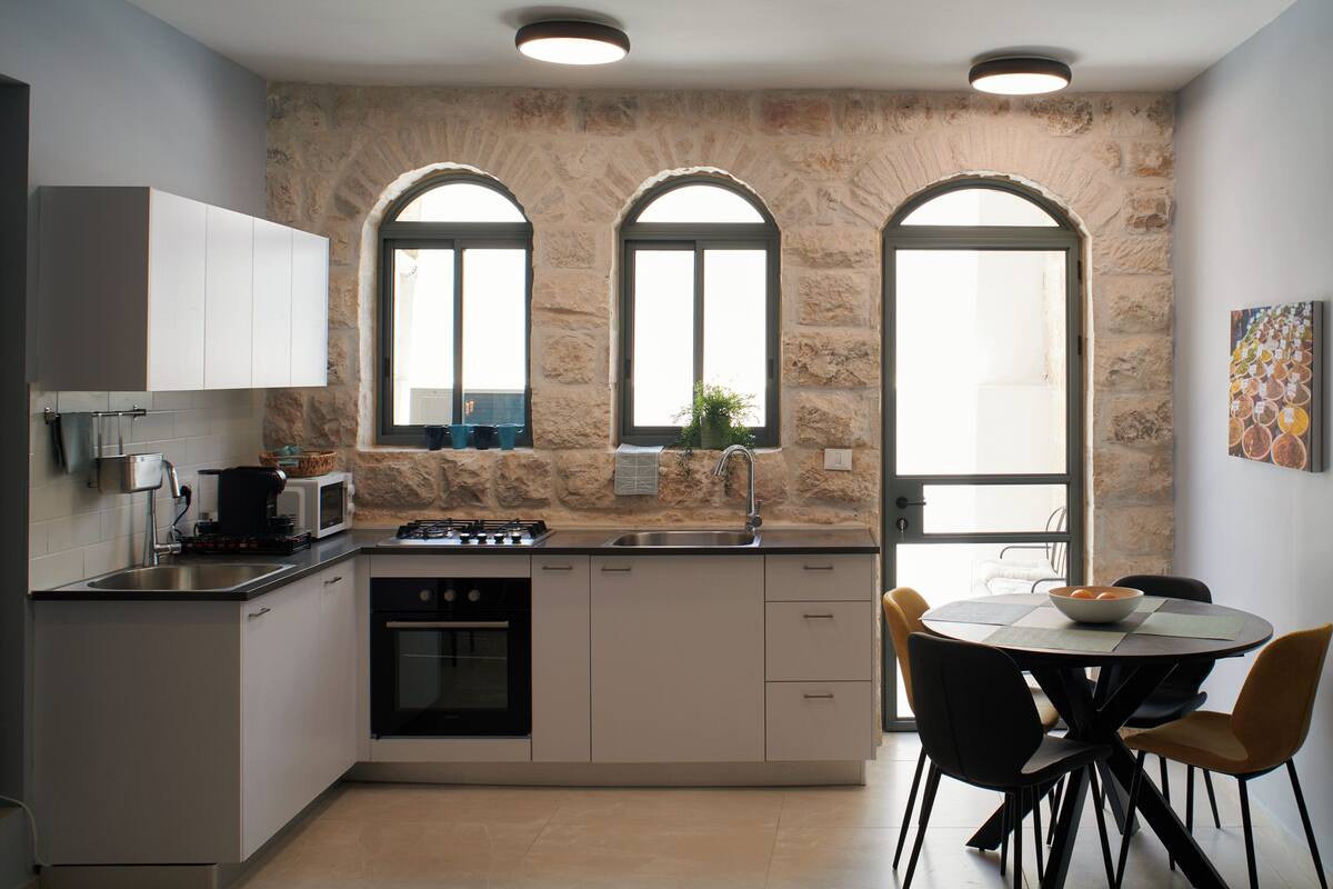 Een moderne keuken met een stenen muur, een eethoek met een ronde tafel en stoelen, en uitzicht door de ramen.