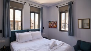 Une chambre d’hôtel avec un grand lit, deux fenêtres avec des rideaux, une petite table, une chaise et un miroir fixé au mur.