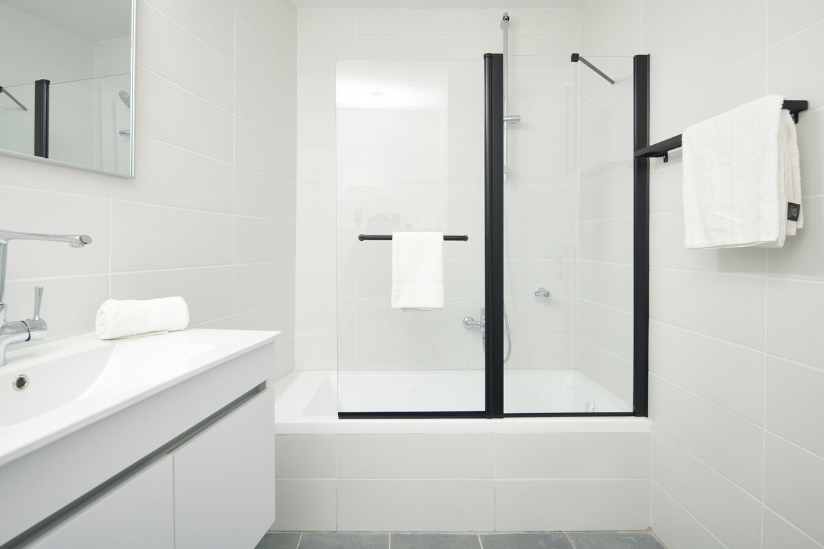 Un baño moderno con ducha de vidrio, una bañera blanca y un espejo grande sobre el lavamanos.