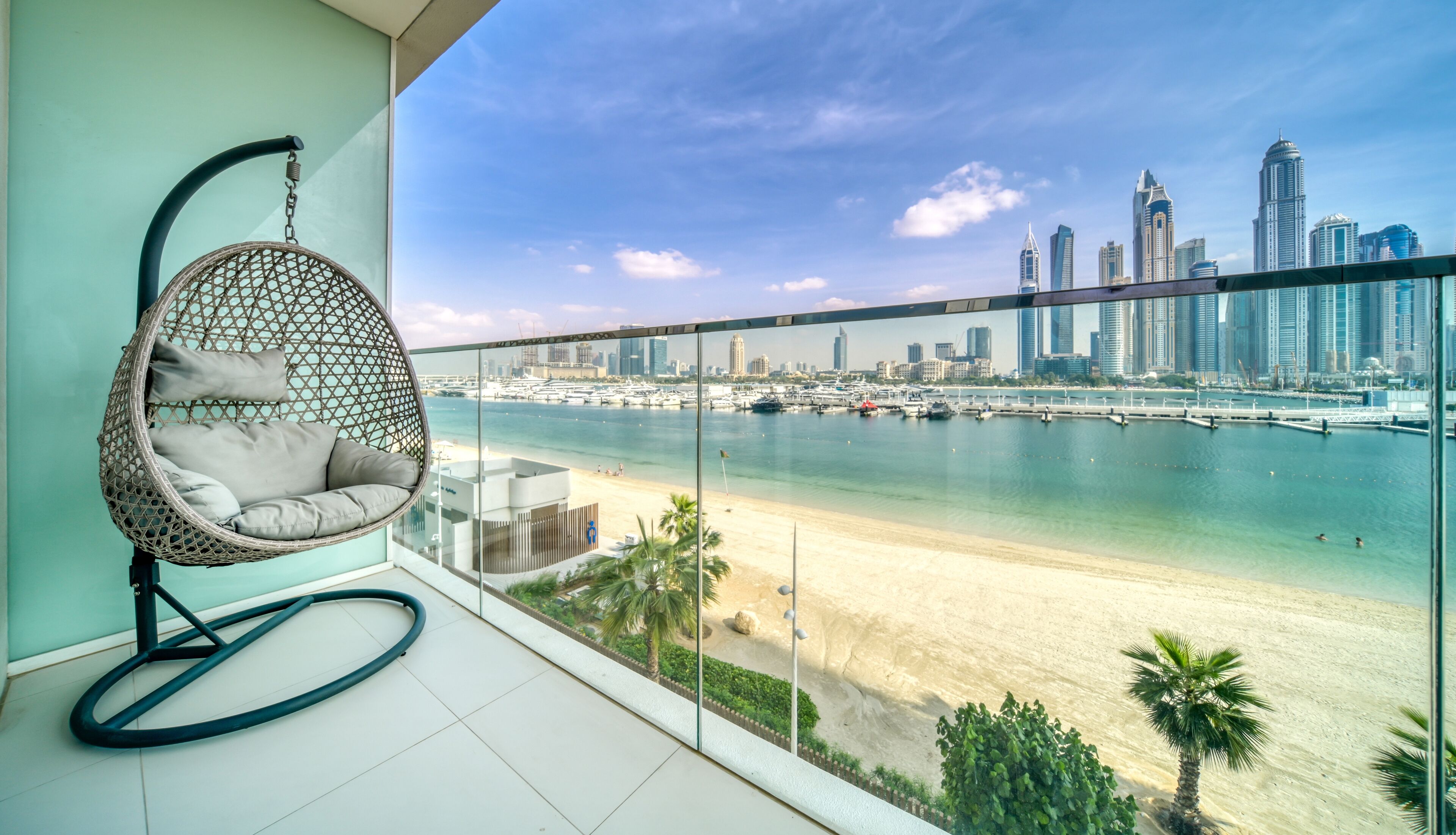 A balcony with a hanging chair overlooking a beach and a city skyline.