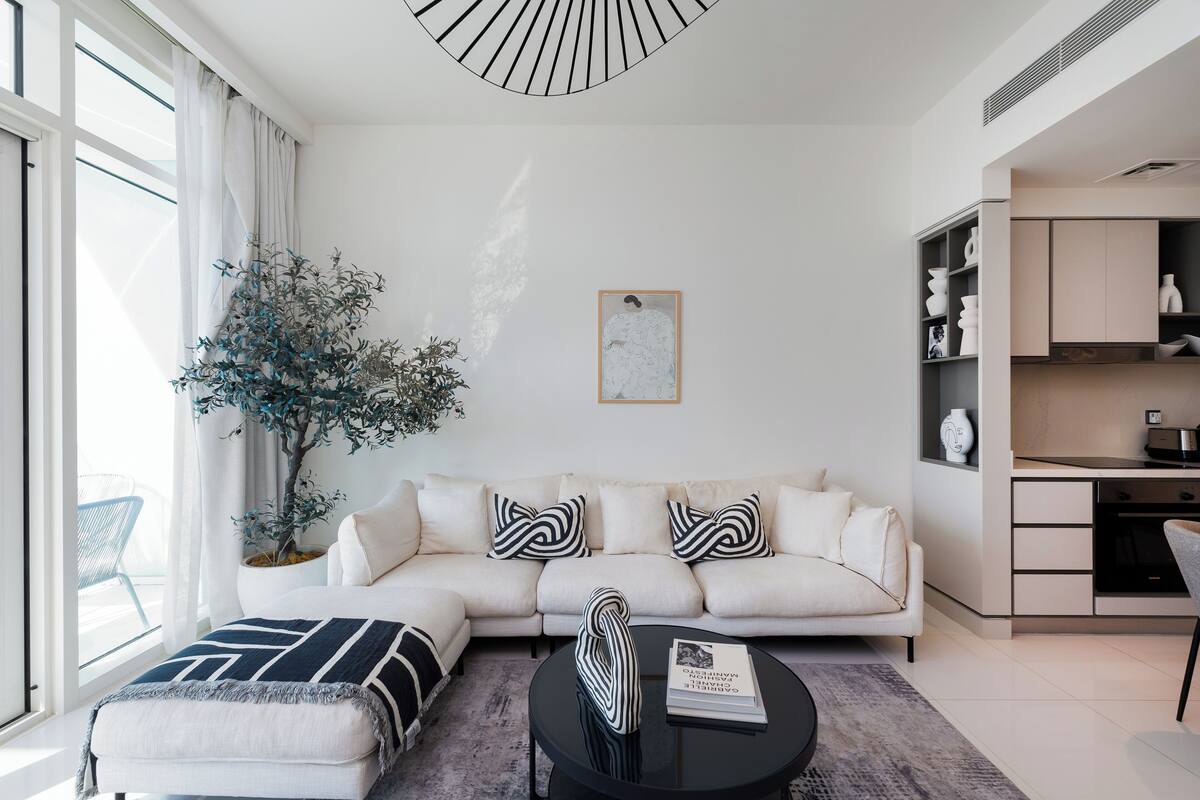Una sala de estar moderna con un sofá blanco, almohadas negras y blancas, una mesa de centro redonda y una planta en maceta.