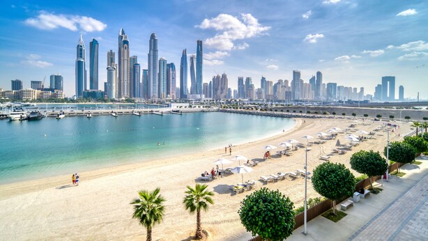 A beach with a marina, palm trees, and a city skyline with modern skyscrapers. - Sunrise Bay - Mint Stay (Dubai)