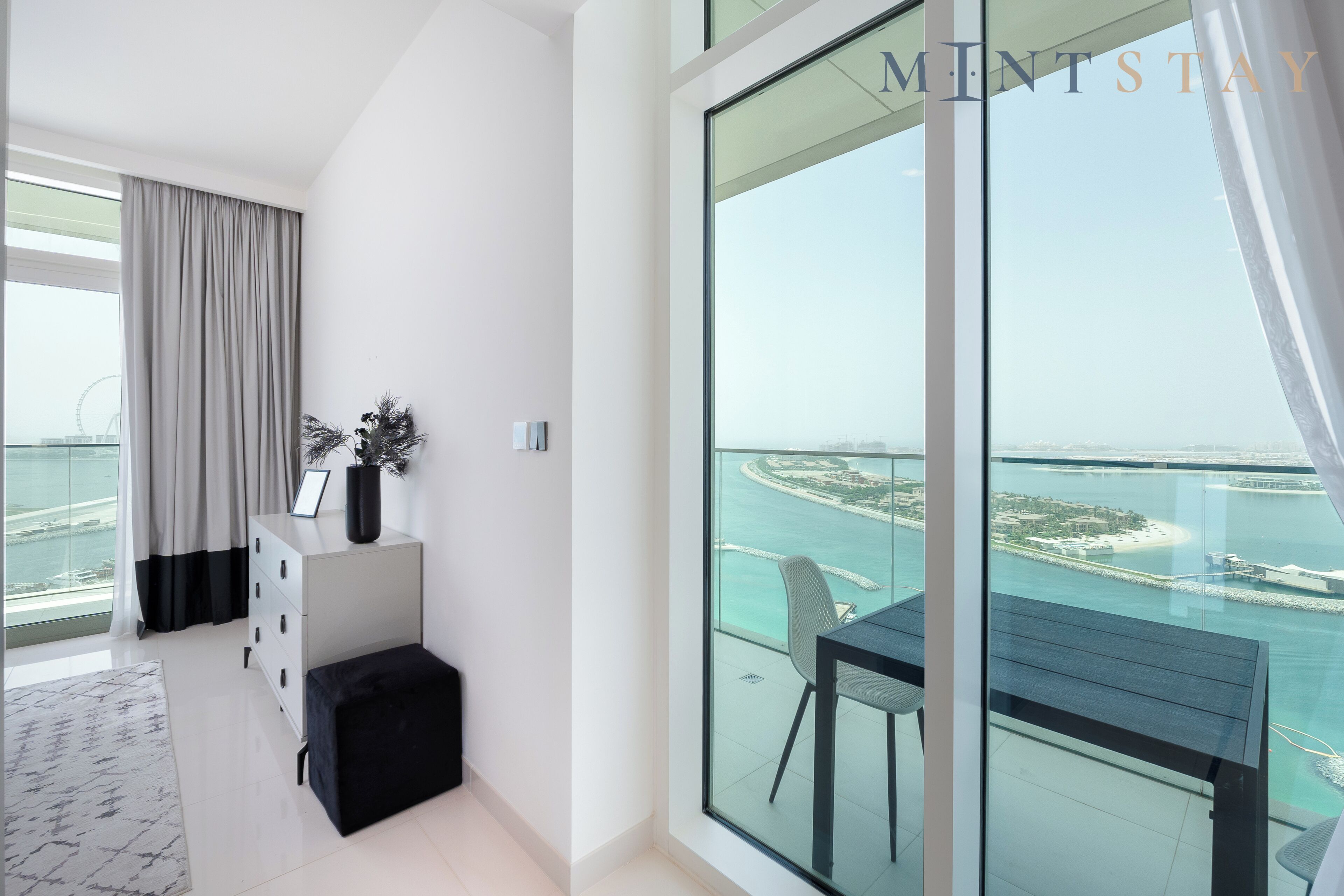 A modern apartment with a large balcony, a view of a coastal area, and a minimalist interior.