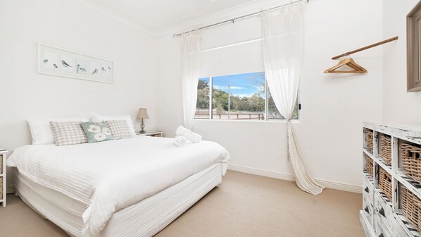 A bedroom with a large bed, a bedside table, a lamp, a window with a view, and a wooden hanger.