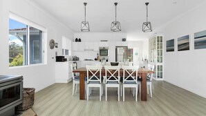 Une cuisine moderne avec des meubles blancs, une table à manger avec des chaises et des luminaires suspendus.