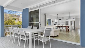 Une vaste terrasse dotée d’une table et de chaises, une cuisine avec des armoires blanches et des appareils en acier inoxydable, et une grande porte-fenêtre coulissante donnant sur un espace extérieur.