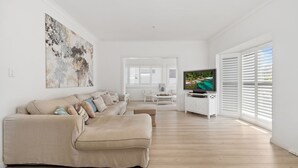 Un salon moderne avec un canapé beige, un téléviseur à écran plat posé sur un meuble blanc et un grand tableau abstrait accroché au mur.