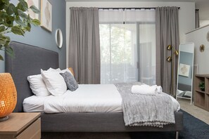 Une chambre à coucher moderne avec un grand lit, des rideaux gris, une lampe de chevet et une vue sur l’extérieur.