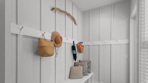 Un pasillo con pared blanca, banco de madera y un perchero con bolsos y un sombrero.