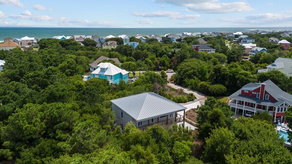 A residential area with houses surrounded by dense greenery, a clear view of the ocean, and a swimming pool visible in the background.