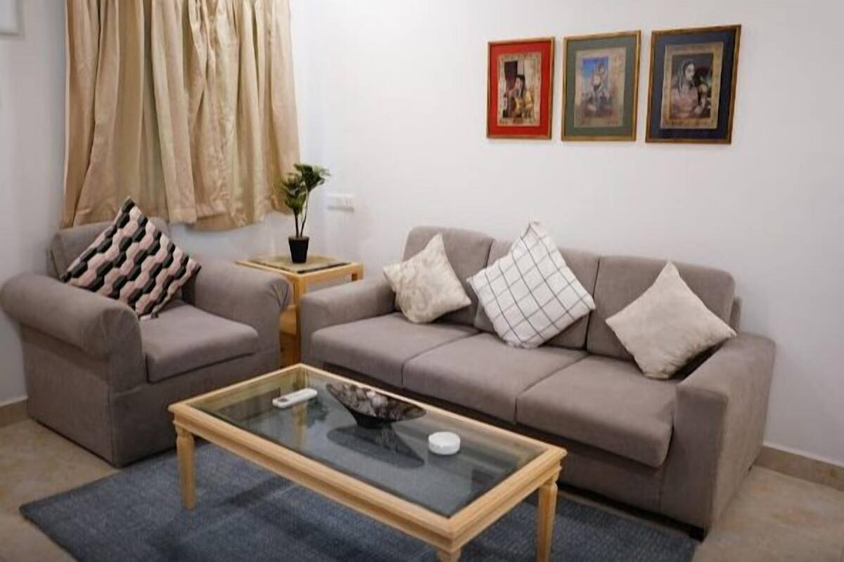 Una sala de estar con un sofá, una mesita de centro de vidrio y una pequeña mesa auxiliar con una planta.
