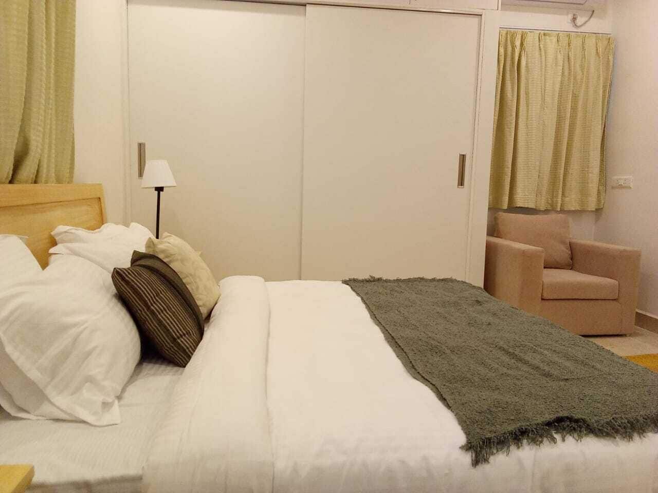 A bedroom with a bed, pillows, a lamp, a chair, and a wardrobe.
