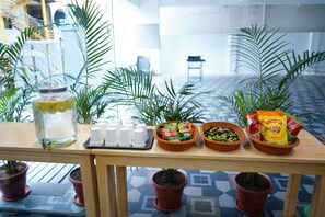 A table with a drink dispenser, cups, snacks, and potted plants. - Enkay Service Apartment (Hyderabad)