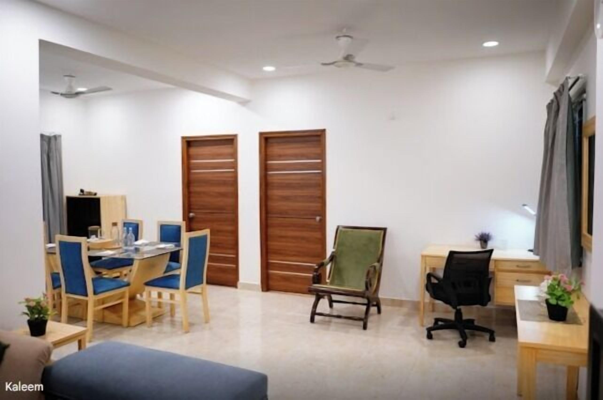 A room with a dining table, chairs, a desk, a computer, and two wooden doors.