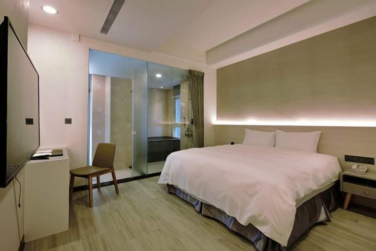 Une chambre d’hôtel équipée d’un lit, d’un bureau, d’une chaise, d’un téléviseur et d’une cloison en verre.