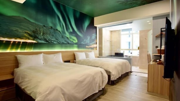 Een hotelkamer met twee bedden, een groot muurschildering en uitzicht op de stad.