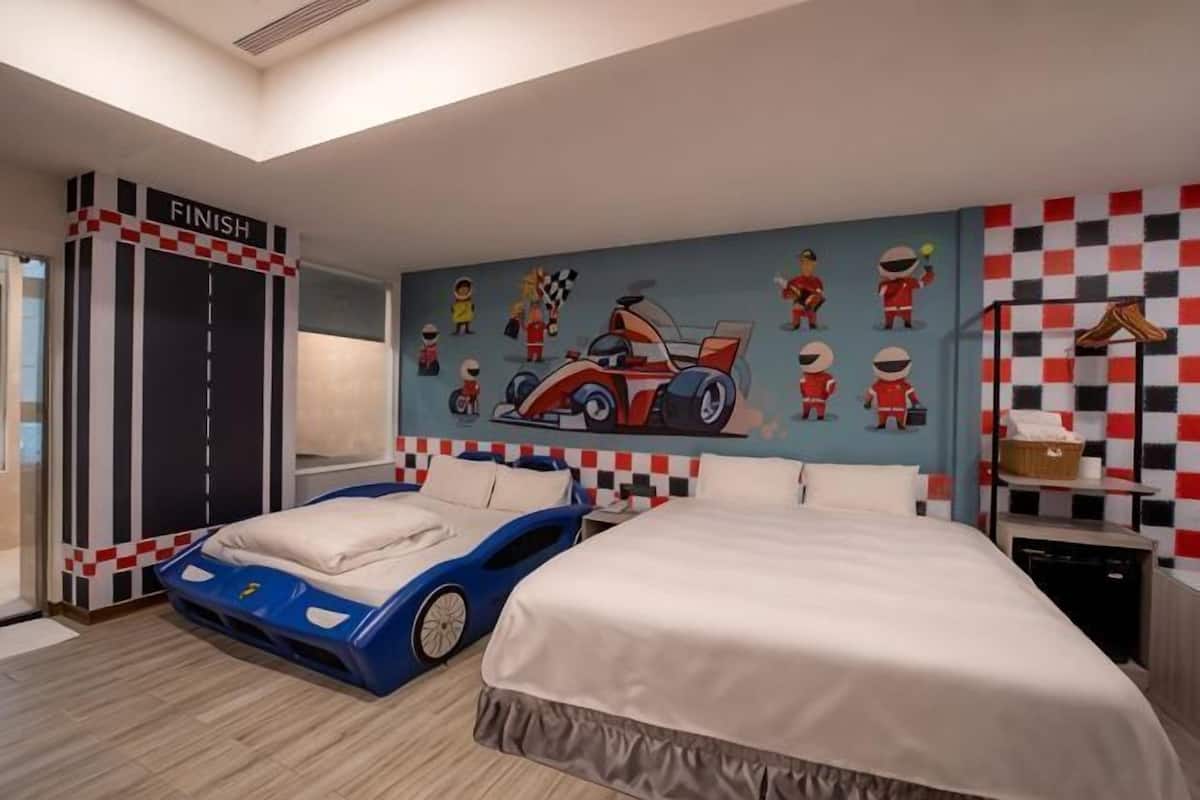 Une chambre à coucher avec un lit, un cadre de lit en forme de voiture de course, une fresque murale représentant des voitures de course et un motif à carreaux sur le mur.