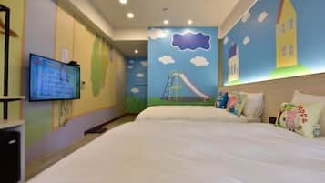 Een kinderkamer met een bed, een televisie en vrolijke wanddecoraties, waaronder een glijbaan en huisjes.