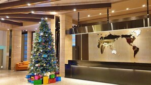 Een receptiehal met een kerstboom en kleurrijke cadeauverpakkingen, een wereldkaart aan de muur en een modern receptiebalie.