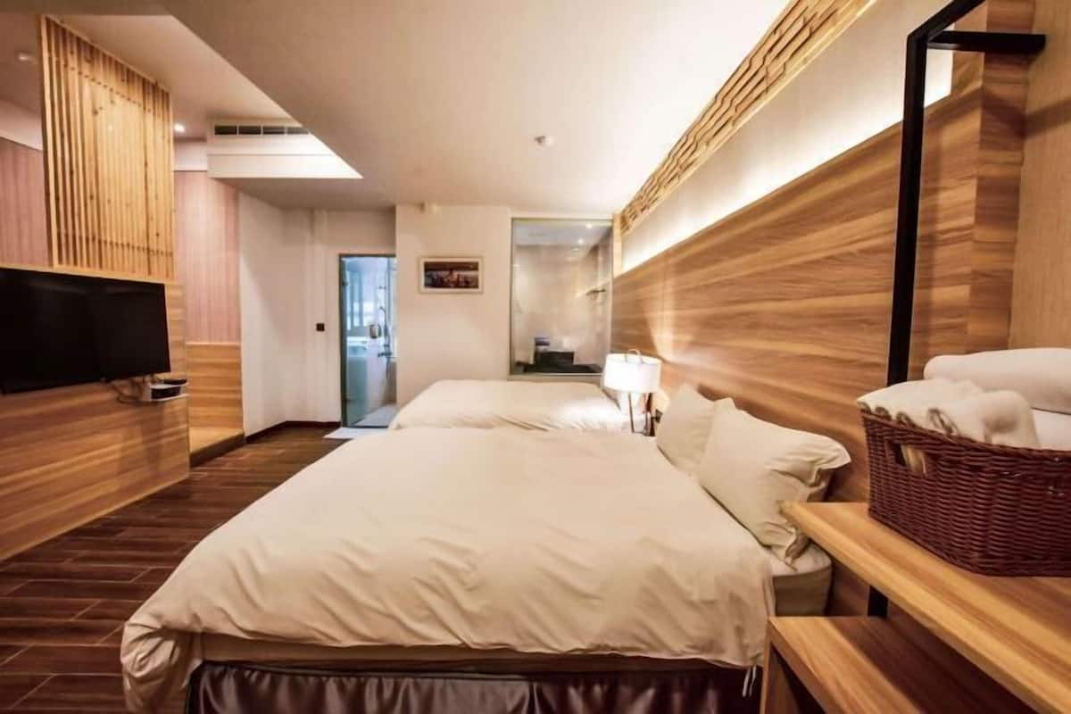 Une chambre d’hôtel comprenant un lit, une télévision, une tête de lit en bois, une table de chevet avec un panier et un miroir.