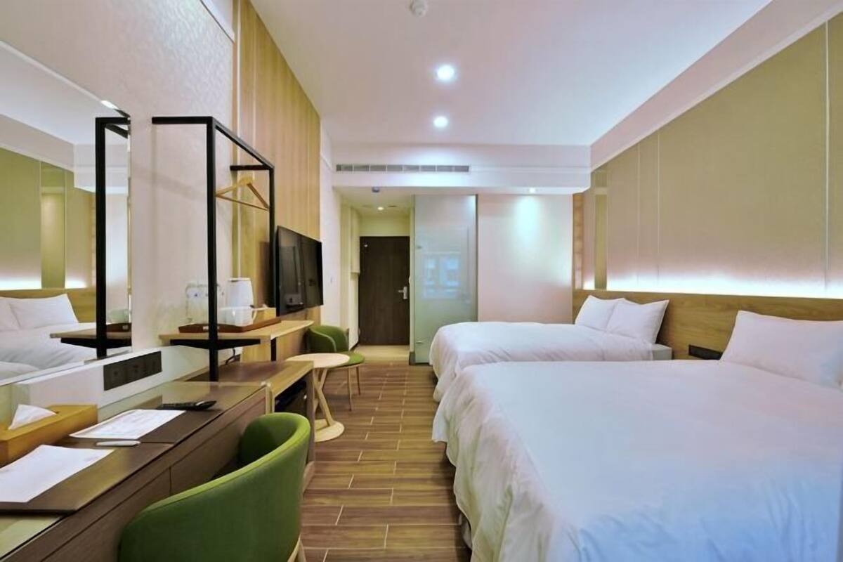 Une chambre d’hôtel avec deux lits, un bureau avec une chaise, une télévision et un miroir.