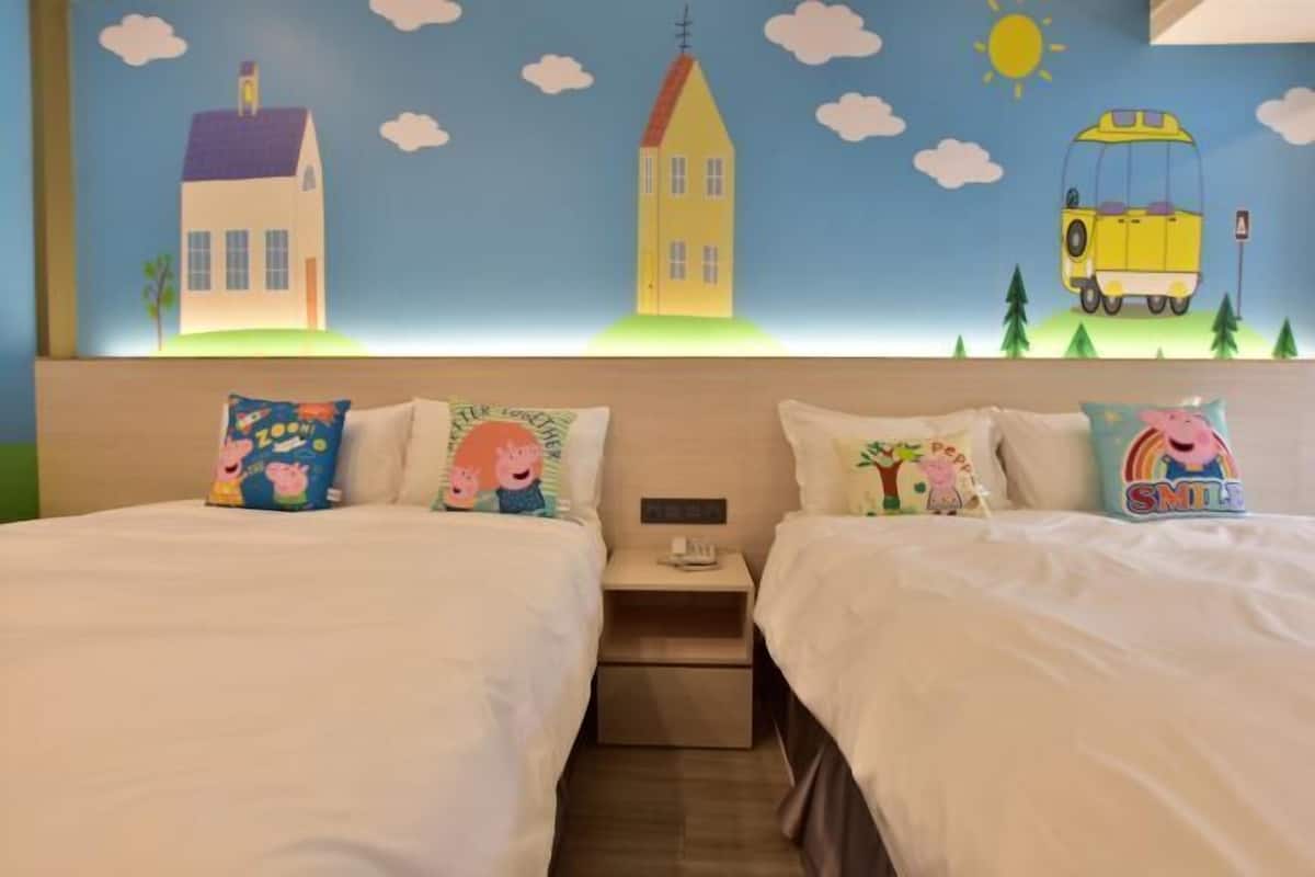 Une chambre d’hôtel avec deux lits, chacun agrémenté d’un oreiller orné d’un personnage de dessin animé. La chambre est décorée d’une fresque murale représentant des maisons, un autobus et un soleil.